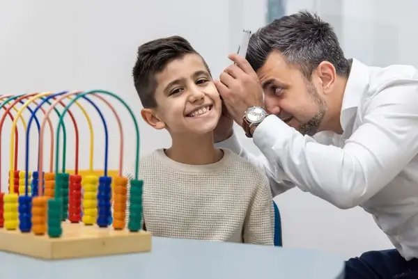 Ein Arzt untersucht das Ohr eines lächelnden Jungen in einer kinderfreundlichen Praxis.